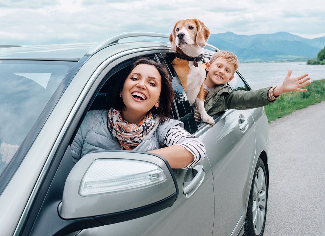 Personal Insurance - Portrait of a Cheerful Mother and Son Traveling in a Car with Their Dog Looking Out the Windows at a Scenic Lake